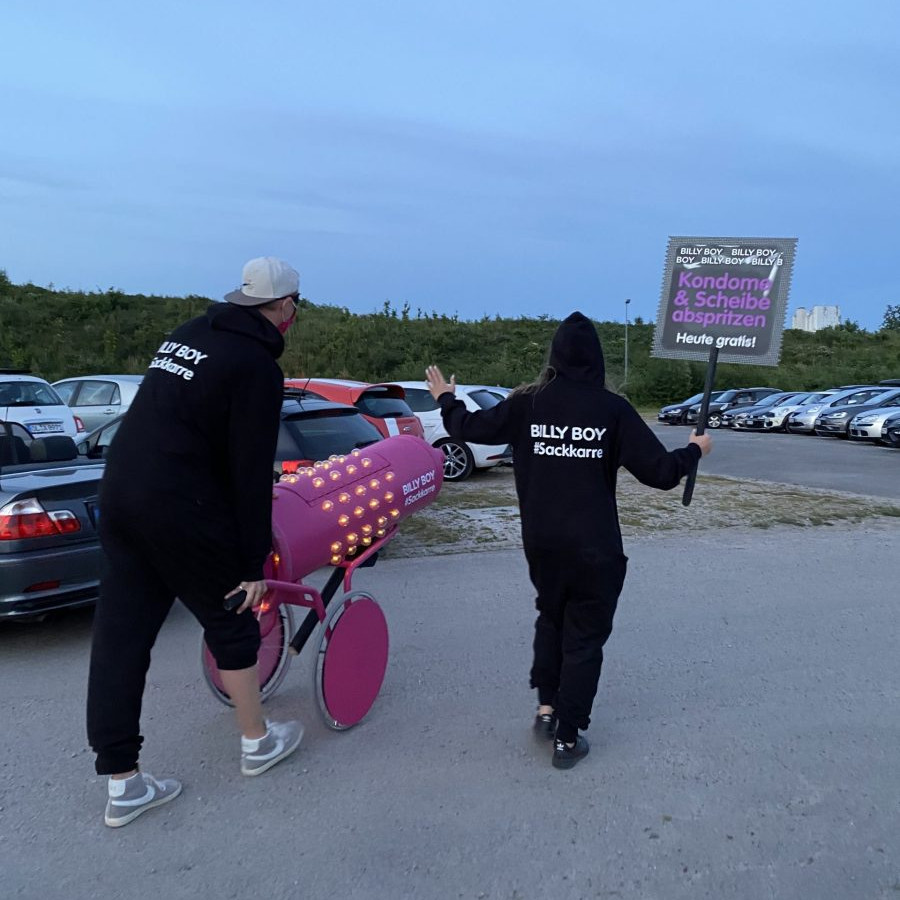 Billy Boy Autokino: Die beiden Promoter gehen mit Sackkarre und Schild auf die parkenden Autos zu.