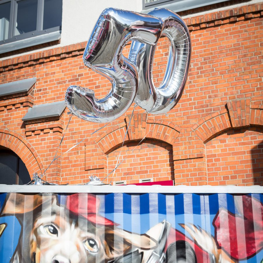 BLG Logistics Jubiläum: Vor dem BLG Forum stehen Container, die bunt besprüht sind. Über den Containern schweben zwei Luftballons die die Zahl 50 ergeben.