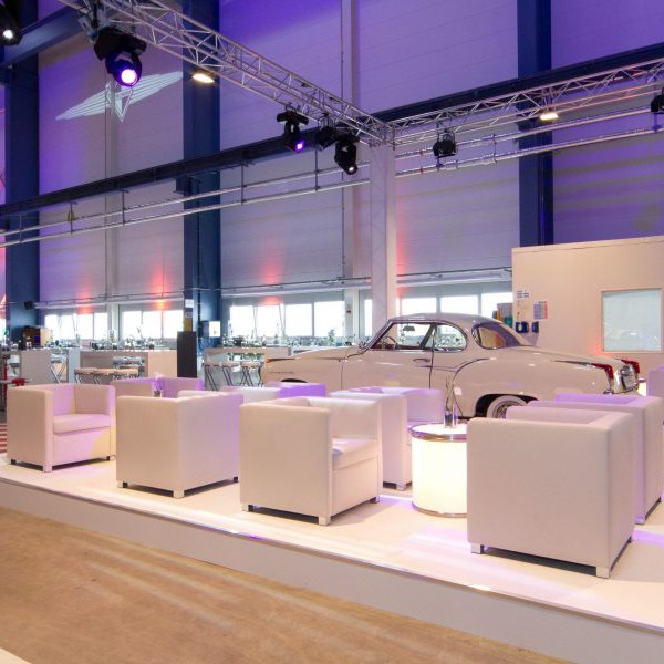 Daimler 75 Jahre PKW: Weiße Ledersessel mit Beistelltisch auf einem Podest. Im Hintergrund steht ein weißer Borgward.