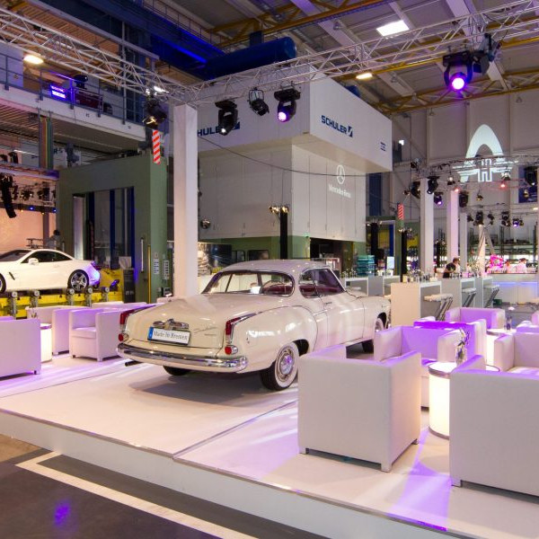 Daimler 75 Jahre PKW: Weiße Ledersessel mit Beistelltisch auf einem Podest. Im Hintergrund steht ein weißer Borgward.