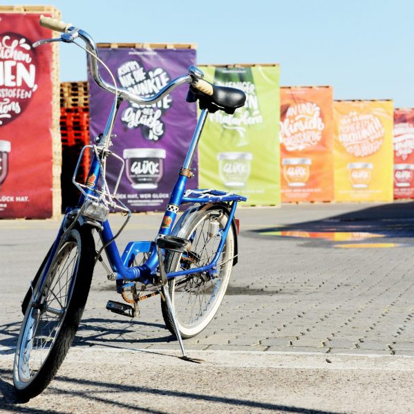Göbber Mitarbeiterfrühstück: Ein Klapprad vor Pallettentürmen an denen Banner hängen