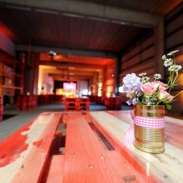Göbber Mitarbeiterfrühstück: Auf einem Pallettenstapen, der als Stehtisch dient, steht eine klaeine Dose in der Blumen stecken.