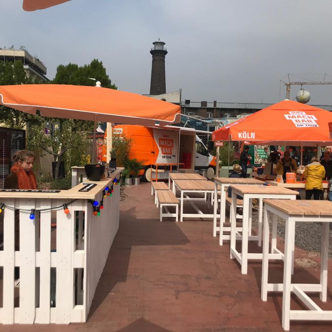OBI MachBar Roadshow: Blick auf die Eventfläche, auf der Stehtische und Sonnenschirme stehen.