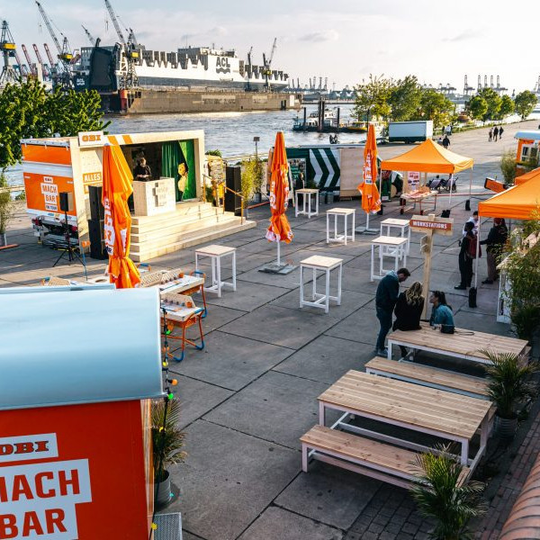 OBI MachBar Roadshow: Eventfläche von oben. Hier gibt es Stehtische, Sonnenschirme, und eine kleine Bühne.