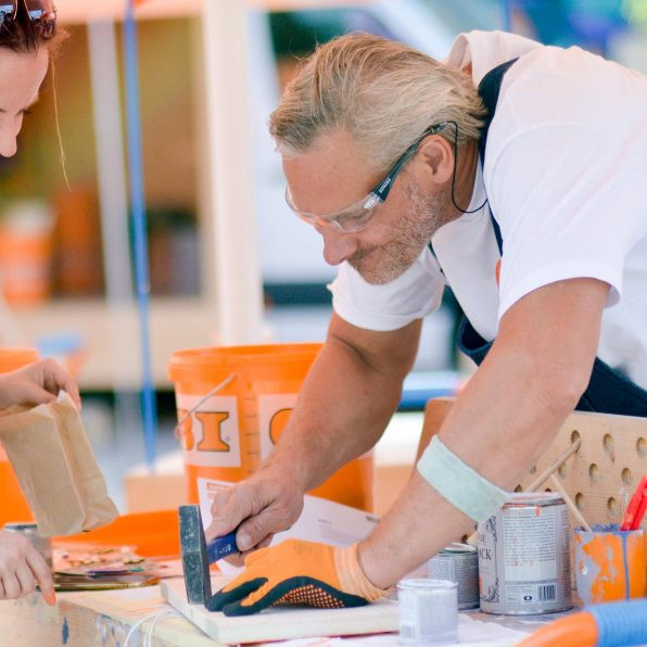 OBI MachBar Roadshow: Ein Obi MachBar Mitarbeiter hilft einer jungen Frau beim zusammenbauen ihres Werkstücks
