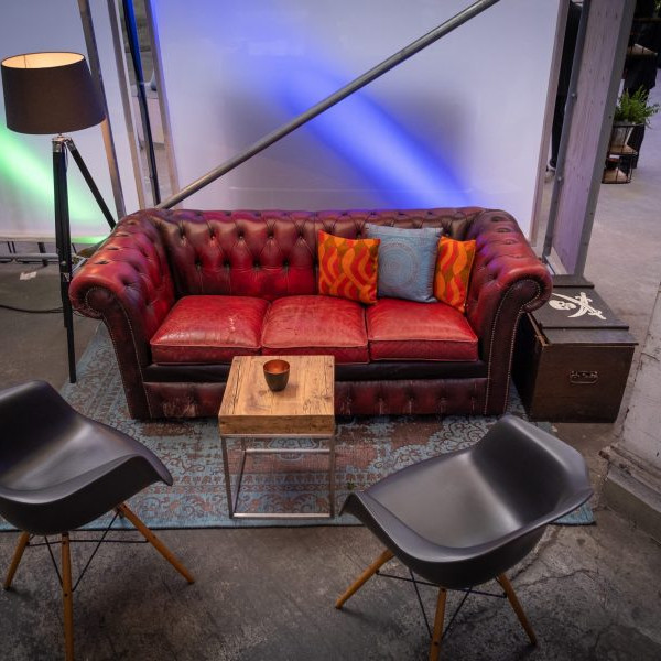Robert C. Spies 100 Jahre: Ein rotes Ledersofa mit Holzbeistelltisch und zwei schwarzen Stühlen.